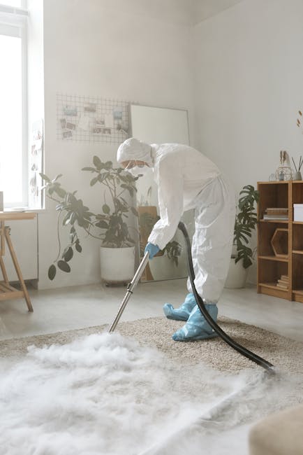 A yellow vacuum cleaner with a black hose and cleaning head is positioned on a decorative woven rug in a living room with wooden flooring. To the left, a wooden sideboard with black metal legs holds a