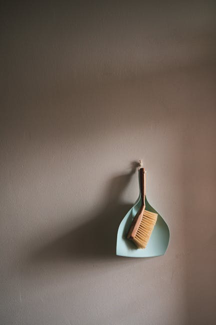 A beige wall with a wall hook holding a small, light blue silicone dish and a natural wood-handled scrub brush with stiff bristles, positioned in a domestic setting. The arrangement appears clean and organized, suitable for surface cleaning or sanitisation routines. The lighting is soft, highlighting the minimal decor. This image reflects general cleaning tools used in the context of a full domestic cleaning or deep cleaning process, as referenced in the Canonbury end of tenancy cleaning checklist Islington guide, provided by Carpet Cleaning Islington.