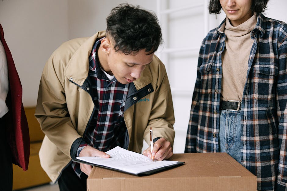 A person in a beige jacket and plaid shirt is focused on signing a document placed on a cardboard box, with a cleaning checklist visible on the page. Next to them, a woman in a plaid shirt and beige turtleneck observes. They are indoors in a well-lit room with neutral-colored walls, and a white spiral staircase is visible in the background. The scene emphasizes surface cleaning and organisation during an end of tenancy process, with attention to detail and cleanliness. This image relates to domestic cleaning and sanitisation services provided by Carpet Cleaning Islington, supporting comprehensive end of tenancy cleaning checklists in Islington.