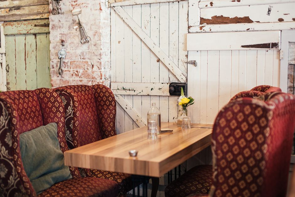 A cozy dining area featuring a wooden table with a natural finish, set against a rustic white wooden door with visible peeling paint and distressed texture. The table is illuminated by soft ambient li